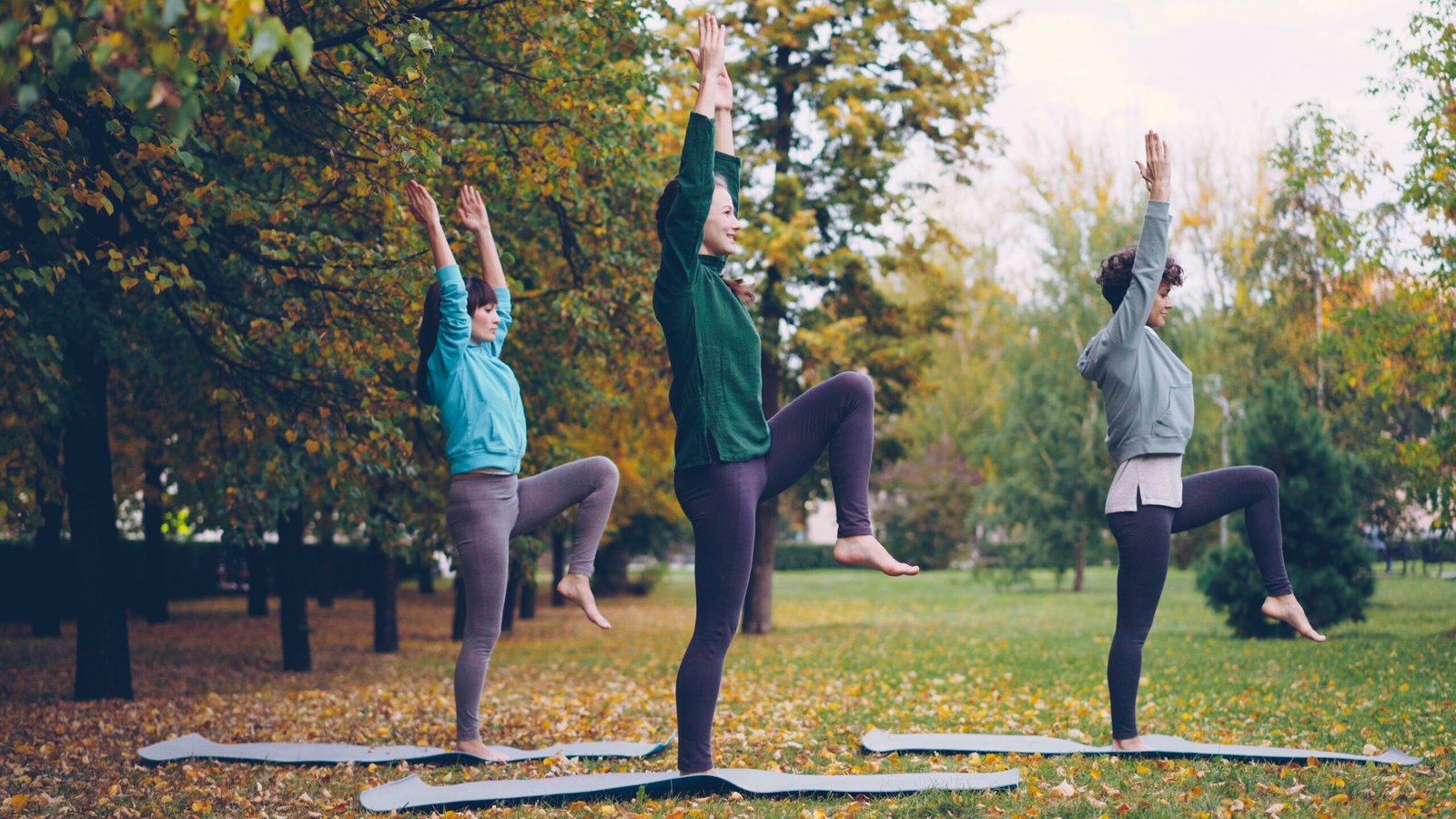 Three women performing yoga poses together outdoors, demonstrating 3 person yoga poses