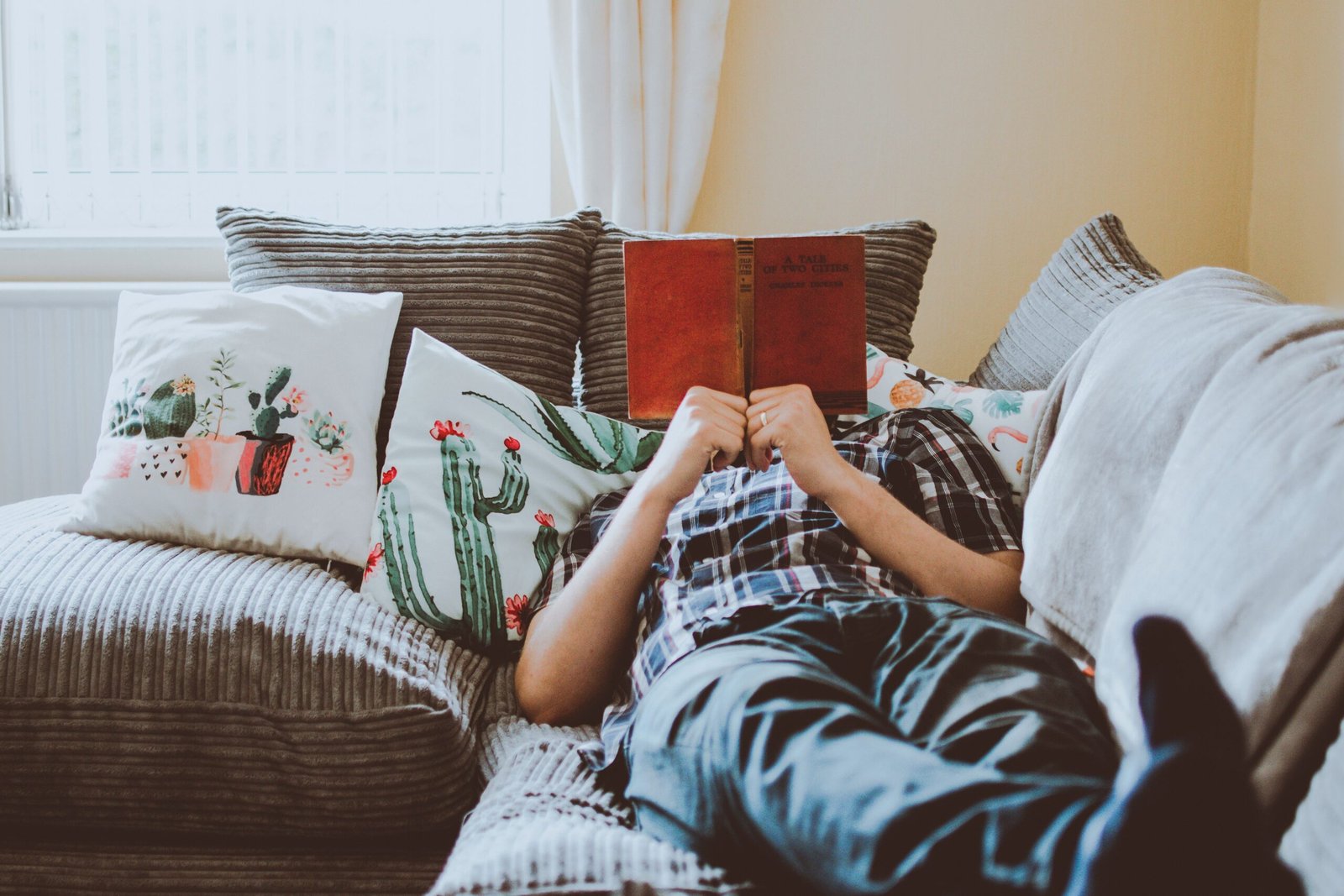 Person relaxing on a sofa reading a physical book, away from screens as part of a digital detox