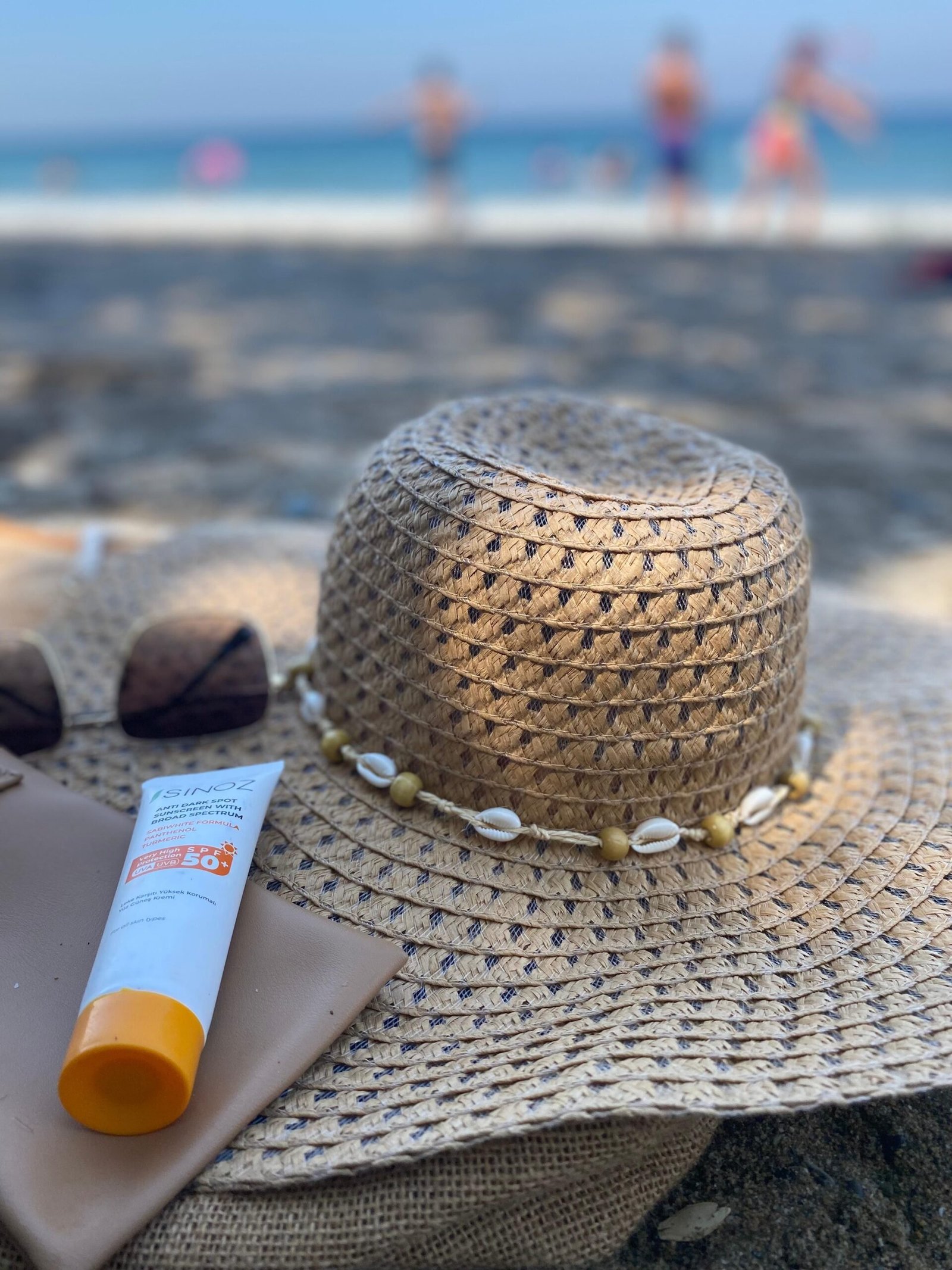 Straw hat and sunscreen bottle on a sandy beach, illustrating the importance of daily SPF protection