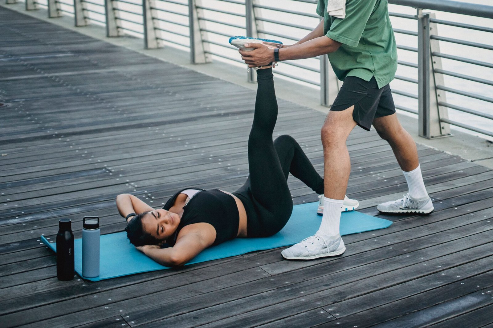 Woman receiving an assisted leg stretch on a yoga mat outdoors to improve flexibility
