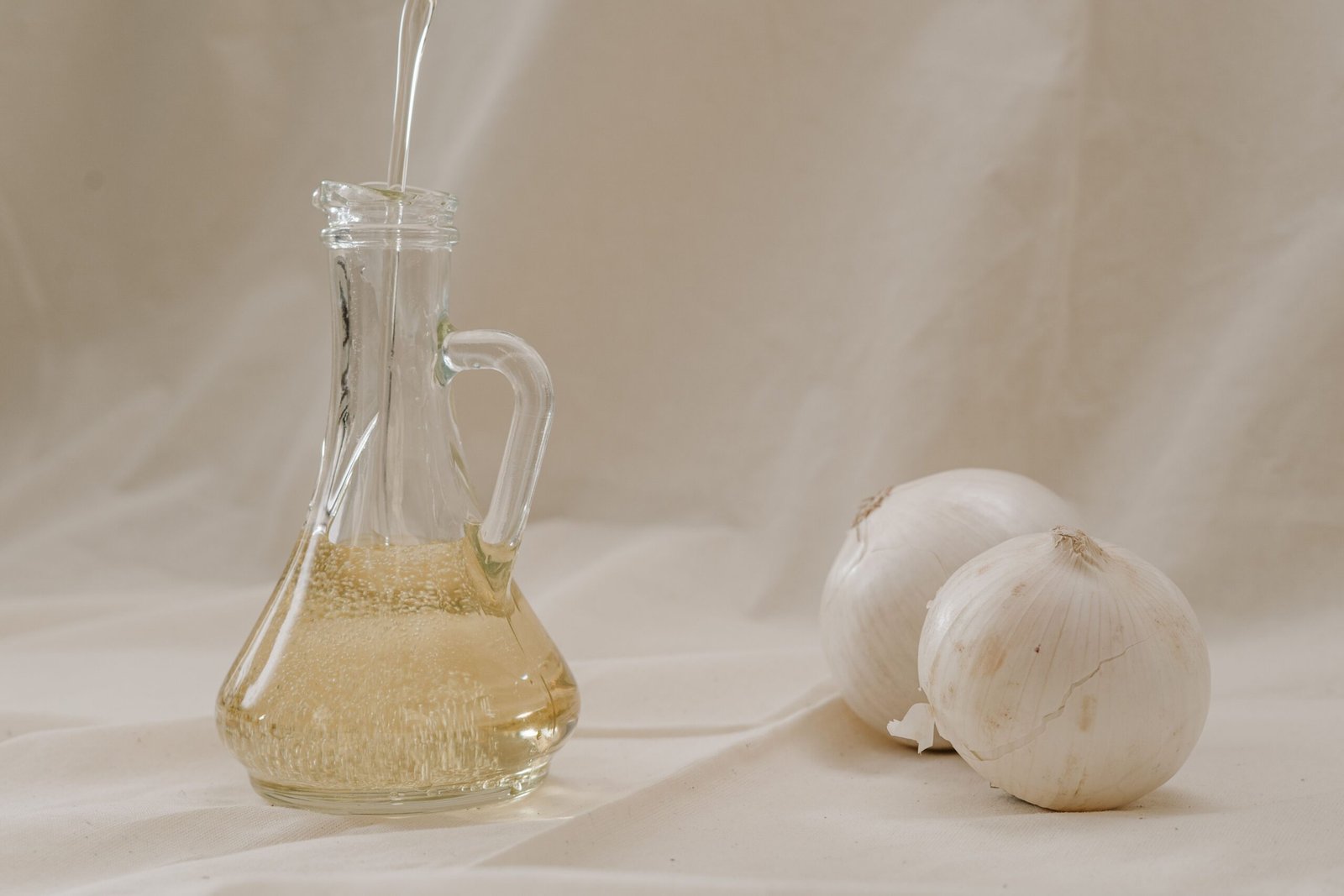 Olive oil being poured into a glass jar alongside garlic, heart-healthy ingredients that support lower cholesterol