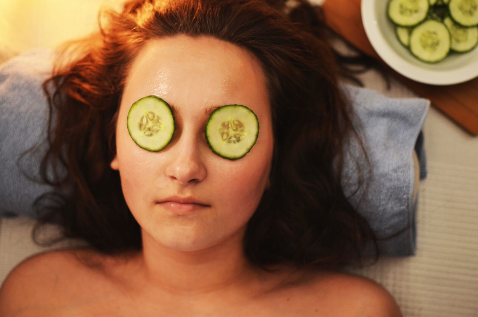 Woman lying down with cucumber slices on her eyes to reduce under-eye puffiness