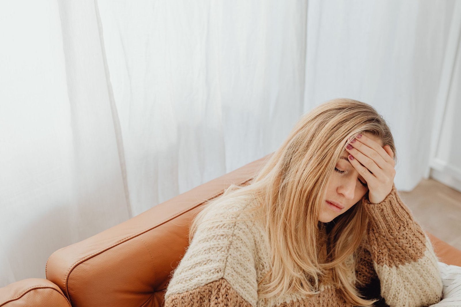Woman sitting on a sofa with eyes closed and hand on forehead, showing signs of emotional exhaustion