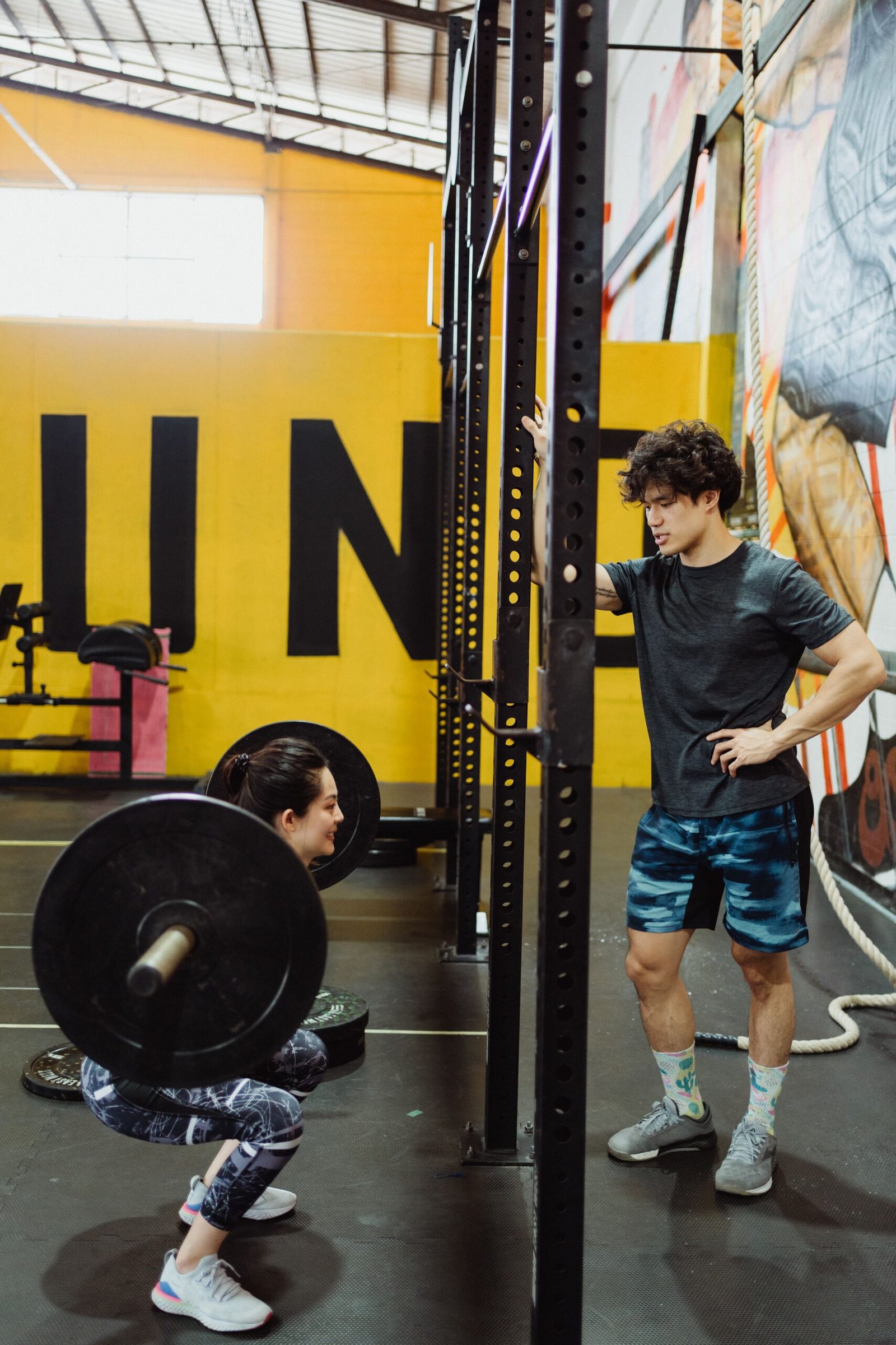 Woman performing a barbell squat with coaching support, demonstrating beginner strength training form
