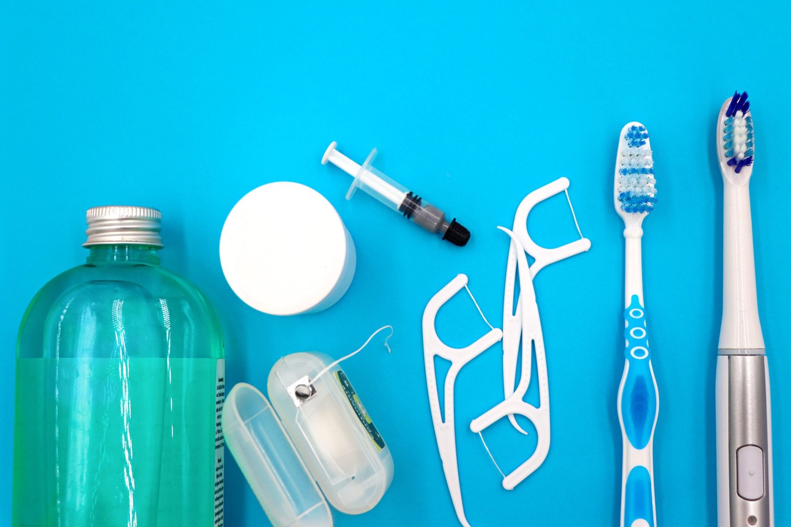 Flat lay of oral hygiene essentials including toothbrushes, floss and mouthwash, used for daily plaque removal